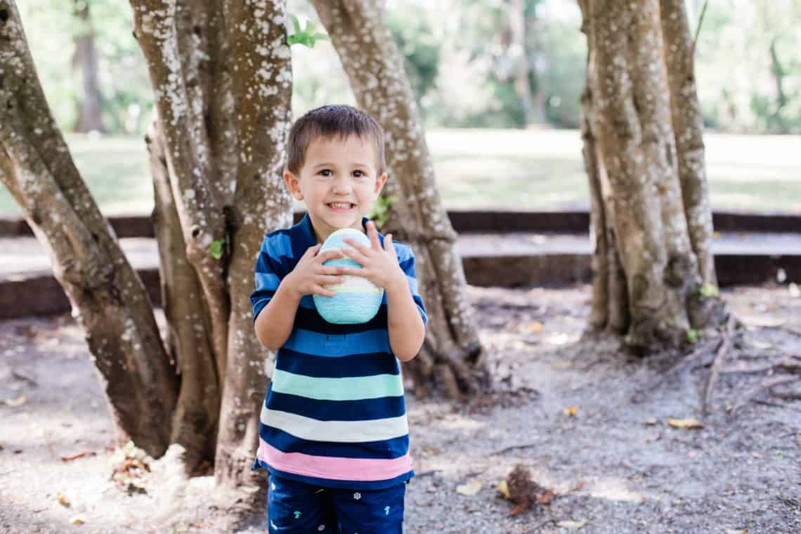 Toddler boy carries an easter egg wearing kids easter outfit striped polo and shorts