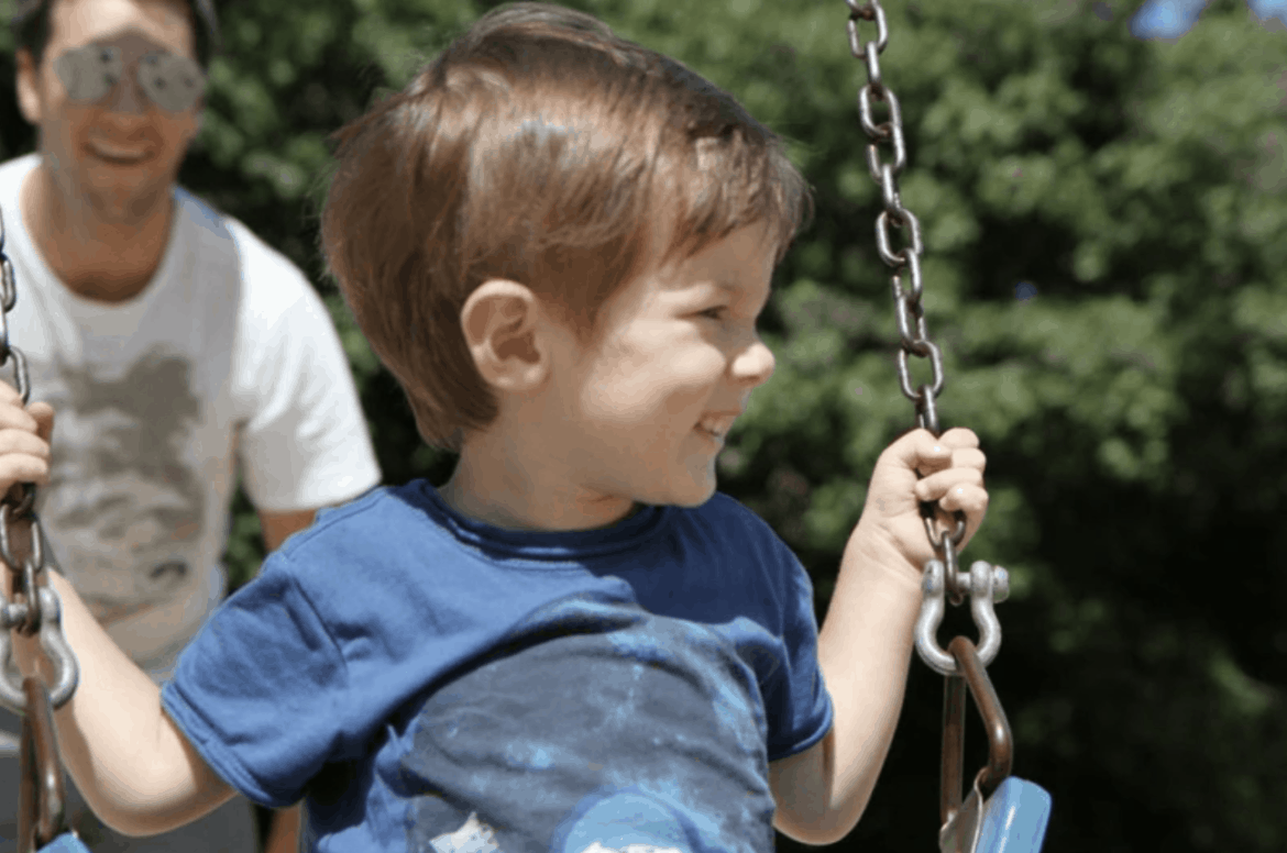 father pushing young boy on swing