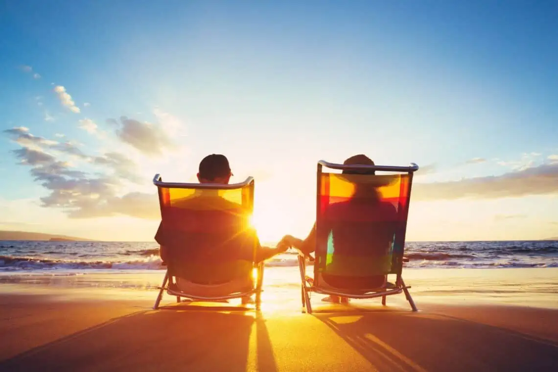 couple sitting in chairs at sunset on the beach holding hands